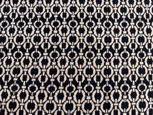 Jacquard-Strickstoff mit ornamentalem Muster in Beige und Schwarz, zusammengerollt und in Nahaufnahme sichtbar